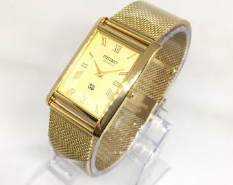 Reloj de pulsera Seiko SQ Quartz Tank vintage: esfera romana dorada, correa de acero inoxidable dorada.