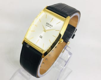 Reloj de pulsera Seiko Barrel Tank vintage con esfera blanca y correa de cuero negra.