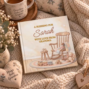 May include: A square hardcover book titled A BLESSING FOR Sarah WITH LOVE FROM GRANDMA, featuring an illustration of a wooden rocking chair, a small stool with baby shoes, a toy train, wooden blocks, and a plush bunny on a round rug.