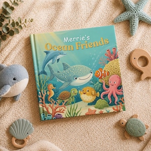 Peut inclure: Un livre carré à couverture rigide intitulé Merrie's Ocean Friends avec une couverture sarcelle illustrant un dauphin, un requin-baleine, un poisson-clown, une pieuvre, une tortue de mer, un hippocampe et un poisson-globe parmi des récifs coralliens.