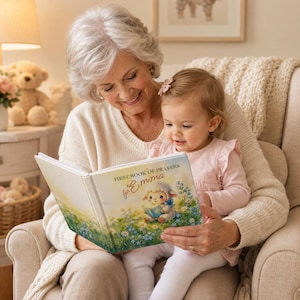 May include: A hardcover book titled First Book of Prayers for Emma, featuring an illustration of a white lamb holding a blue book in a field of green grass and blue flowers, with a white background and gold lettering on the front cover.