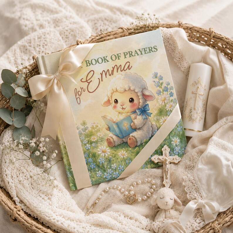 May include: A hardcover book titled MY BOOK OF PRAYERS for Emma featuring a cartoon lamb illustration, tied with a cream satin ribbon. Included are a white pillar candle with a gold cross, a silver crucifix, a pearl rosary, and a small plush lamb.