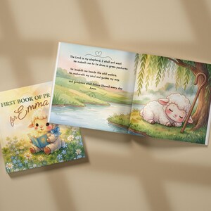 May include: A children's book titled First Book of Prayers for Emma featuring a cover illustration of a lamb reading a book in a field of flowers and an open page showing a sleeping lamb under a tree with the text The Lord is my shepherd.