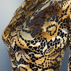 May include: A long-sleeved garment with a high neckline, featuring a detailed pattern in shades of brown, black, and gold. The fabric has a textured appearance, with a design reminiscent of animal print.