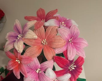 May include: A bouquet of handmade flowers in shades of pink, red, and white. The flowers have a textured, velvet-like appearance with detailed centers. The arrangement is held together with green stems, creating a vibrant floral display.