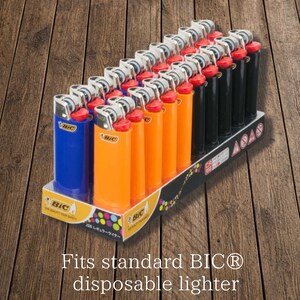 K&ouml;nnte beinhalten: Eine Auslage mit blauen, orangefarbenen und schwarzen BIC Einwegfeuerzeugen. Die Feuerzeuge haben silberne Metalloberteile und rote Z&uuml;ndkn&ouml;pfe. Die Auslage tr&auml;gt das BIC-Logo und den Text "Fits standard BIC disposable lighter".