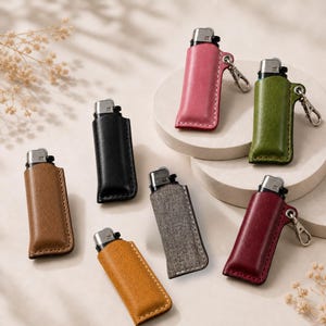 K&ouml;nnte beinhalten: Eine Auswahl an Feuerzeugen in Lederetuis. Die Etuis sind in verschiedenen Farben erh&auml;ltlich, darunter Braun, Schwarz, Rosa, Gr&uuml;n, Grau, Orange und Burgunderrot. Einige Etuis haben einen Metallclip. Die Feuerzeuge sind auf neutralem Hintergrund angeordnet.