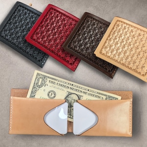 Puede incluir: Una colección de carteras de cuero en varios colores: negro, rojo, marrón y beige. Cada cartera presenta un patrón de calaveras repetido. Una cartera marrón claro con un billete de dólar en primer plano.