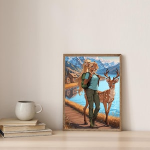 May include: A framed art print featuring a woman with deer-like features standing next to a deer. The artwork depicts a serene lakeside scene with mountains in the background. The woman wears a blue shirt, green pants, and a backpack.