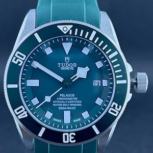Puede incluir: Un reloj Tudor Pelagos con esfera y bisel verdes. El reloj tiene una caja de acero inoxidable y una correa de caucho verde. La esfera presenta marcadores y agujas blancas, con una ventana de fecha. Resistente al agua hasta 500m.
