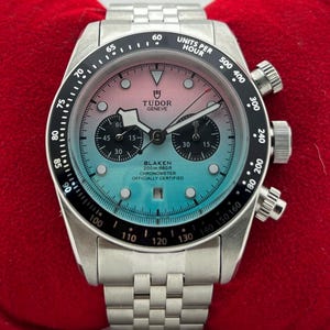 May include: A stainless steel Tudor Geneve chronograph watch with a pink and blue gradient dial, black sub-dials, and a black tachymeter bezel. The dial features the text Tudor Geneve, Blaken, 200m 660ft, Chronometer, and Officially Certified.