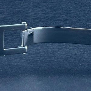 May include: A close-up of a stainless steel watch clasp, with the brand name "TUDOR GENEVE" and "SWISS MADE" text. The clasp is open, showing the inner workings and the brushed metal finish. The watch band is also visible.