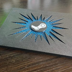 Könnte beinhalten: Eine rechteckige schwarze Schaumstoffplatte mit einem zentralen, kreisförmigen weißen Steam-Logo. Der Schaumstoff weist einen sternförmigen Ausschnitt auf, der eine leuchtend blaue, texturierte Netzschicht darunter freilegt.