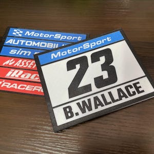 May include: Two rectangular racing-style decals with black borders. The top decal features the text MotorSport, AUTOMOBILI, sim, ASSETTO, iRacing, and RACEROOM. The bottom decal displays the text MotorSport, the number 23, and B.WALLACE.