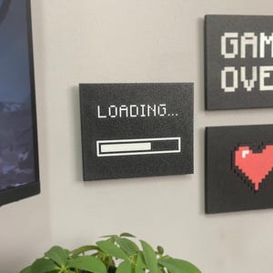May include: Three rectangular wall plaques with a black textured finish. One plaque displays the white text LOADING... with a progress bar. Another features the white pixelated text GAME OVER. The third shows a red pixelated heart icon.