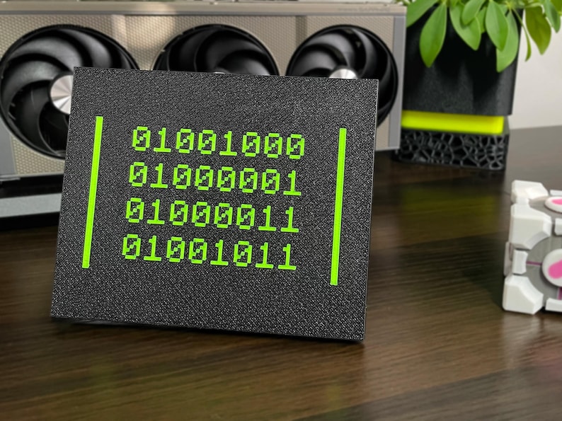 Neon-green HACK binary plaque displayed upright on a black desk stand.
