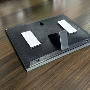 Rear of the plaque with desk stand, keyhole and adhesive mounting strips.