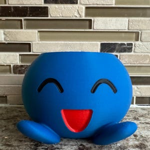 May include: A white ceramic mug with a black handle and the text "But First, Coffee" in a black, handwritten-style font. The mug is on a white surface.