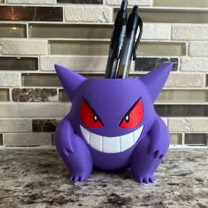 May include: A white ceramic mug with a black handle and the text "But First, Coffee" in a black, handwritten-style font. The mug is on a white surface.