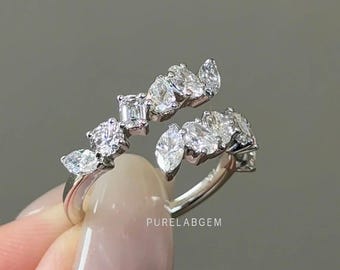 May include: A silver-toned open bypass ring featuring a series of marquise, round, and emerald-cut clear stones arranged along two curved bands. The metal band is polished and reflective. The text PURELABGEM is printed on the inner band surface.