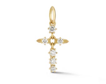May include: A gold cross pendant featuring a vertical row of three round clear stones and a horizontal bar with one round clear stone on each side. The cross is suspended from a small gold jump ring at the top, showcasing a polished metal finish.