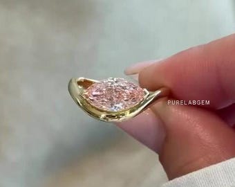 May include: A gold ring featuring a marquise-cut light pink gemstone set in a smooth, curved bezel setting. The metal band has a polished finish and the text PURELABGEM is visible on the side of the setting, showcasing a refined and elegant design.