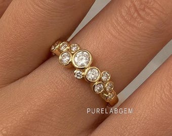May include: A gold ring featuring a cluster of multiple round, bezel-set clear stones of varying sizes arranged in a staggered, organic pattern along the band. The text PURELABGEM is printed in small white letters near the base of the ring.
