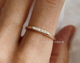 May include: A gold band ring featuring five small, round, clear stones set in a horizontal row along the top surface. The metal has a polished finish, and the text PURELABGEM is visible in small white letters near the base of the ring band.