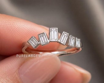 May include: A silver-toned ring featuring five baguette-cut clear stones arranged in a graduated fan shape. The stones are set in a bezel style along the top of the band. The text PURELABGEM is printed in small white letters below the ring.