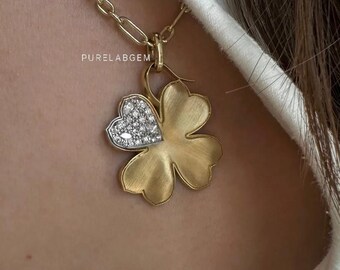 May include: A gold-toned necklace featuring a four-leaf clover pendant with a brushed matte finish. One leaf of the clover is shaped like a heart and is encrusted with small clear stones. The text PURELABGEM is visible above the pendant.