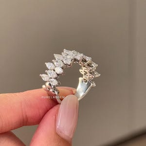 Pode incluir: Anel de prata com uma s&eacute;rie de pedras preciosas transparentes com corte marquesa dispostas em um padr&atilde;o curvo. O anel tem uma banda de prata. O texto "PURELABGEM" &eacute; vis&iacute;vel no anel.