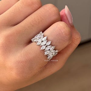 Pode incluir: Um anel de prata com uma s&eacute;rie de pedras de corte marquesa dispostas em um padr&atilde;o repetitivo. O anel &eacute; cravejado com v&aacute;rias pedras preciosas transparentes. O texto "PURELABGEM" &eacute; vis&iacute;vel.