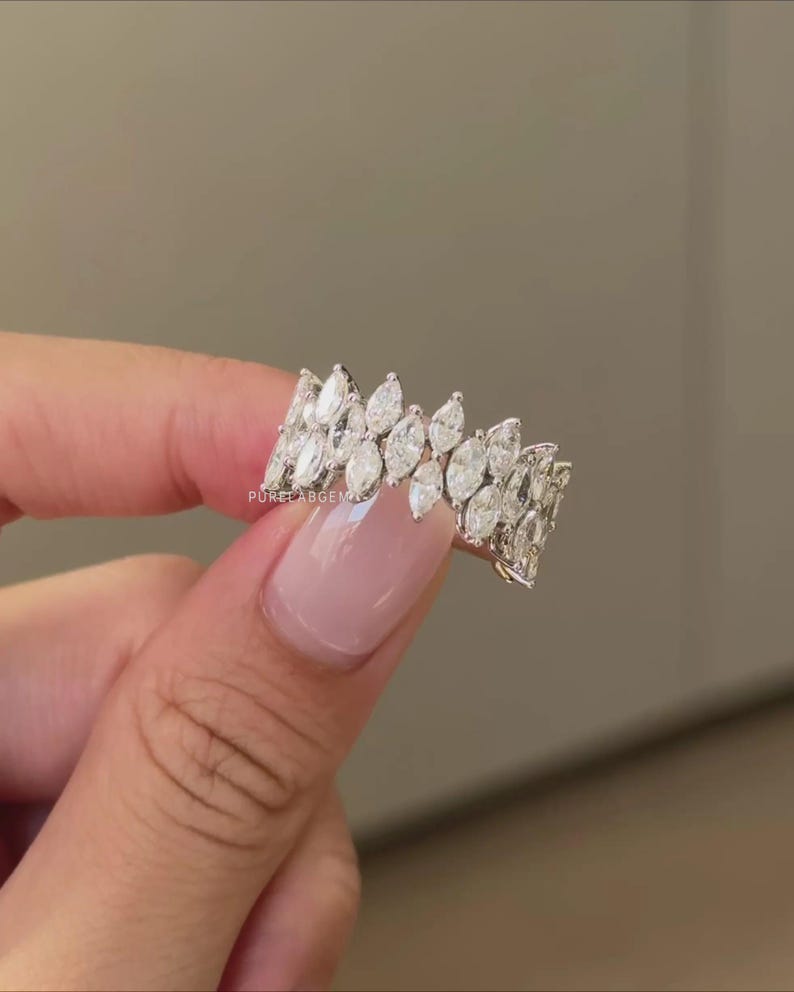 Pode incluir: Um anel de ouro branco com uma dupla fileira de diamantes em corte marquise. Os diamantes s&atilde;o colocados pr&oacute;ximos uns dos outros, criando uma faixa cont&iacute;nua e brilhante. O anel &eacute; exibido em um fundo neutro.