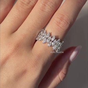 Pode incluir: Um anel de ouro branco com m&uacute;ltiplos diamantes de corte marquesa dispostos em um padr&atilde;o semelhante a folhas. O anel &eacute; usado em um dedo, mostrando seu design intrincado e brilho. O anel &eacute; uma joia.