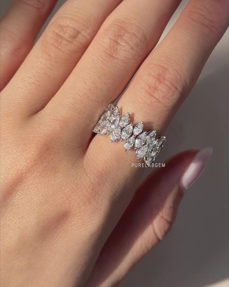 Pode incluir: Um anel de ouro branco com m&uacute;ltiplos diamantes de corte marquesa dispostos em um padr&atilde;o semelhante a folhas. O anel &eacute; usado em um dedo, mostrando seu design intrincado e brilho. O anel &eacute; uma joia.