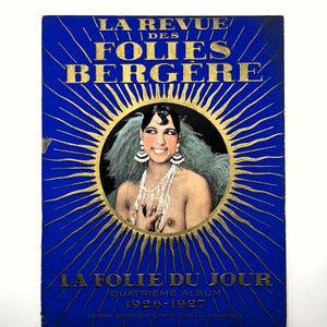 Può includere: Un poster vintage con sfondo blu e scritte dorate. Il testo recita "LA REVUE DES FOLIES BERGERE" e "LA FOLIE DU JOUR". Una donna con capelli scuri, orecchini e collana è al centro. Il poster è del 1926-1927.