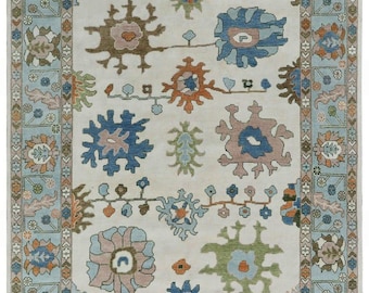 May include: Rectangular area rug with a cream-colored field and a light blue border. The rug features floral and geometric patterns in shades of blue, brown, orange, and green. The design includes stylized flowers and repeating border motifs.