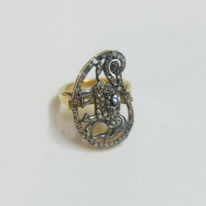 Peut inclure: Une bague en or avec un motif ajouré décoratif. La bague présente un groupe central de petites pierres scintillantes, entouré d'un motif en filigrane. L'anneau de la bague est en or poli simple.