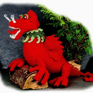 May include: A knitted red dragon with a green and white collar, wings, and black claws. The dragon is posed on a log with a green plant in the background. The dragon has white smoke-like details coming from its nostrils.