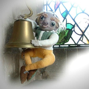 May include: A knitted doll figure with a green and white sweater, yellow trousers, and brown shoes, holding a brass bell. The background features a stained-glass window, adding a touch of colour to the scene.