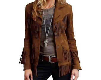May include: Brown suede jacket with fringe detailing. The jacket features a classic collar, button closure, and pockets. The fringe is along the sleeves, chest, and back. The jacket is paired with a gray t-shirt, a silver necklace, and a brown belt.