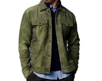 Könnte beinhalten: Olivgrüne Wildlederjacke mit Knopfverschlüssen, zwei Brusttaschen und einem Kragen. Die Jacke wird über einem blauen Button-Down-Hemd und einem marineblauen Pullover getragen. Die Jacke hat ein leicht abgenutztes Aussehen.