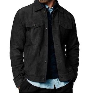 May include: A black suede jacket with two chest pockets and button fastenings. The jacket features a classic collar and is worn over a blue button-down shirt and a dark sweater. The jacket's design is a timeless style.