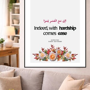 May include: Framed wall art with the text "Indeed, with hardship comes ease" in English and Arabic script. The artwork features a floral arrangement of roses and foliage at the bottom. The frame is black.