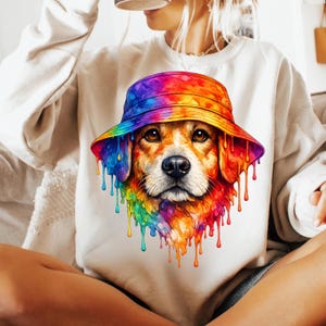 May include: A white sweatshirt featuring a colorful graphic of a dog wearing a tie-dye bucket hat. The dog's fur and the hat are painted with vibrant rainbow colors, with paint drips cascading down the design. The sweatshirt is a casual, comfortable style.