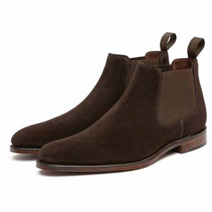 May include: A pair of brown suede Chelsea boots. The boots feature a rounded toe, elastic side panels, and pull tabs. The soles are a darker brown with a light brown edge.