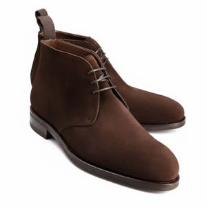 May include: A pair of brown suede chukka boots. The boots have a rounded toe, a lace-up closure, and a pull tab at the back. The soles and heels are a darker shade of brown.