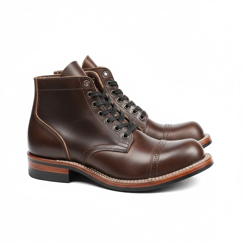 May include: A pair of brown leather boots with a cap toe design. The boots have black laces, a stacked heel, and a stitched sole. The leather has a polished finish, and the boots are set against a white background.