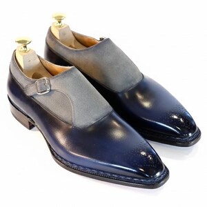 May include: A pair of blue leather dress shoes with a grey suede vamp and a silver buckle closure. The shoes have a pointed toe and are displayed on wooden shoe trees.