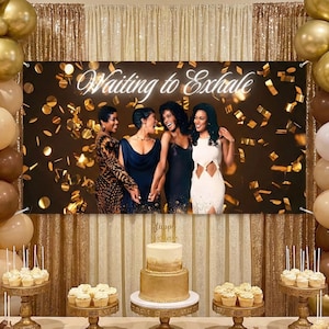 May include: A banner with the text "Waiting to Exhale" above a group of women. The banner is set against a backdrop of gold confetti and a gold curtain. A two-tiered cake and cupcakes are on display.